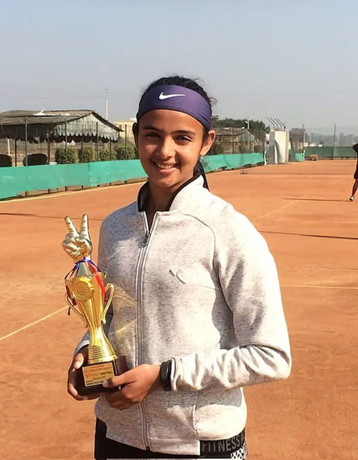La joven pro de tenis profesional sonriendo en la cancha de arcilla sosteniendo un trofeo, destacando la controversia del ego masculino en los deportes.