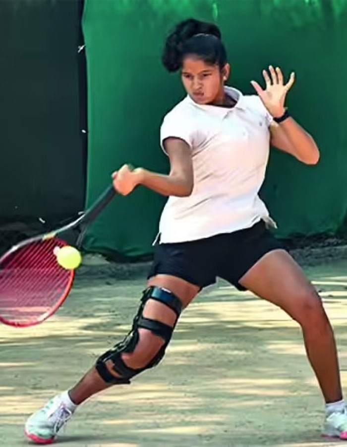 La joven profesional de tenis que usa una rodilla golpeando un disparo de revés en una cancha de arcilla al aire libre durante la práctica.