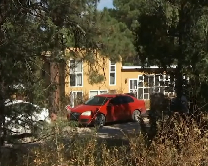 El automóvil rojo estacionado frente a una casa amarilla rodeada de árboles en una escena relacionada con la investigación del crimen familiar.