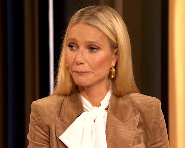 Gwyneth Paltrow con un blazer marrón y una blusa blanca, pareciendo emocional mientras habla de su amistad tóxica con Madonna.
