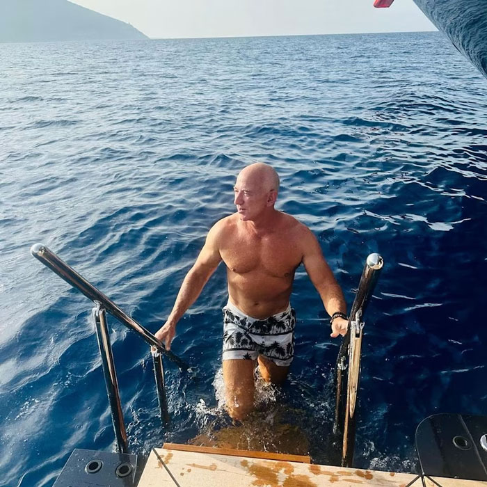 Jeff Bezos mostrando un nuevo aspecto con el cabello, saliendo del océano hacia un bote en un día soleado.