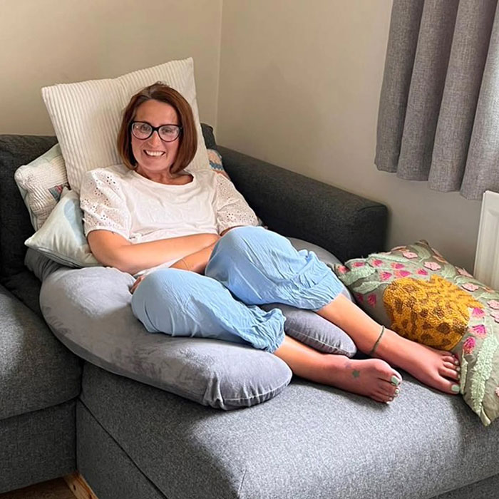 Mujer sonriendo y relajándose en un sofá con almohadas, representando al grupo de apoyo que rompió el silencio después de que la mujer terminó la vida de hambre.