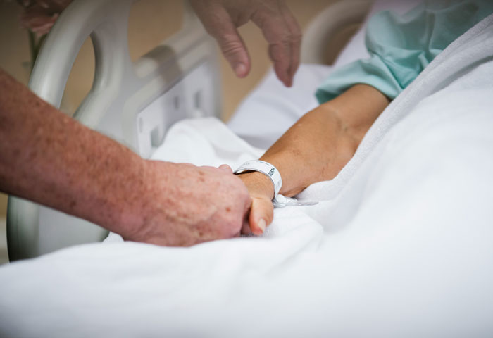 Manos de miembro del grupo de apoyo que sostiene la muñeca de la mujer en la cama del hospital después de que terminó su propia vida de hambre.