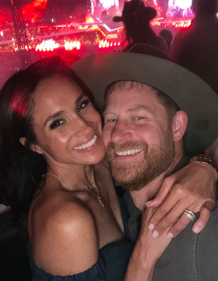 Pareja sonriendo de cerca en un concierto con vibrantes luces de escenario rojo, insinuando el ex sutil jab sutil asistente de Kate Middleton.