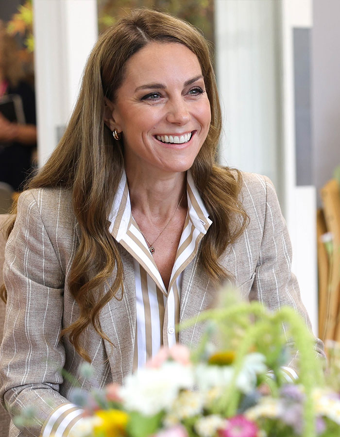 La ex amable de Kate Middleton sonríe durante un compromiso público, con una camisa a rayas y un blazer ligero.