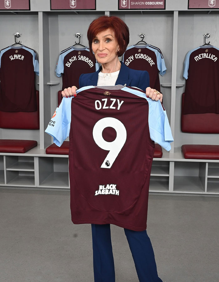 Sharon Osbourne sosteniendo una camiseta de fútbol Ozzy personalizada en un vestuario con Black Sabbath y Ozzy Osbourne Chishs colgando.