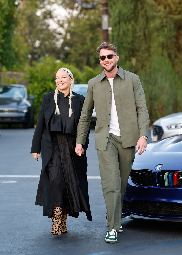 Una modelo y una estrella australiana que se toman de la mano al aire libre, sonriendo casualmente cerca de autos estacionados, relacionado con la campaña de correo electrónico de Netflix.