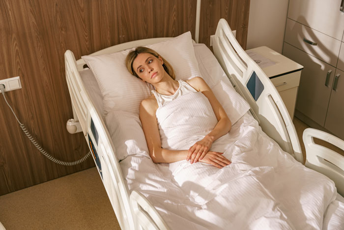 Mujer joven que yace herida en una cama de hospital se veía reflexiva después de emborracharse y herido antes de un plan de ruptura.