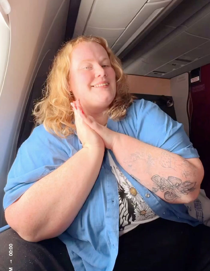 Viajero de talla grande sonriendo en el avión, compartiendo razones para no reservar dos asientos de la aerolínea, enfrentando críticas.