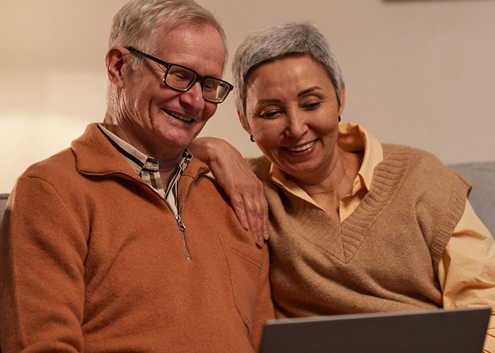 Pareja mayor sonriendo y mirando una computadora portátil juntos, discutiendo a los padres modernos y reacciones mixtas en línea.