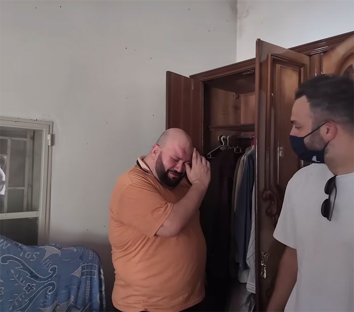El hombre con camisa naranja reacciona emocionalmente mientras visita la casa familiar 46 años después de que papá se fue, mostrando un descubrimiento aturdido.