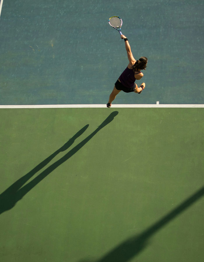 Tennis Pro en acción alcanzando un servicio en la cancha, destacando la carrera deportiva de una joven atleta femenina.