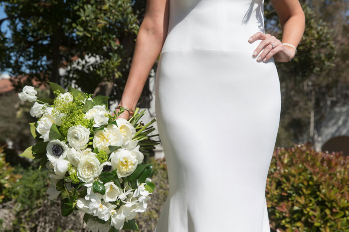 Novia con un vestido de novia blanco que sostiene un ramo de flores blancas durante una lucha de poder en el evento de boda.
