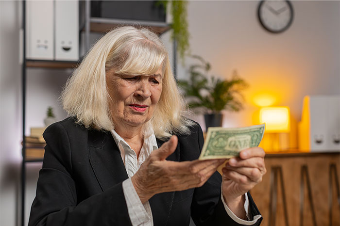 Mujer anciana que inspecciona el billete de dólar, que ilustra el comportamiento derecho después de la disputa de pago del alquiler con nuera.