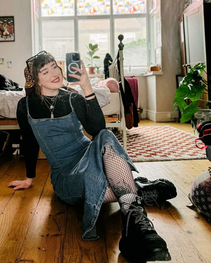 Persona sentada en el piso de madera tomando una selfie en una habitación, mostrando los encubrimientos del artista del tatuaje que se volvieron virales en línea.