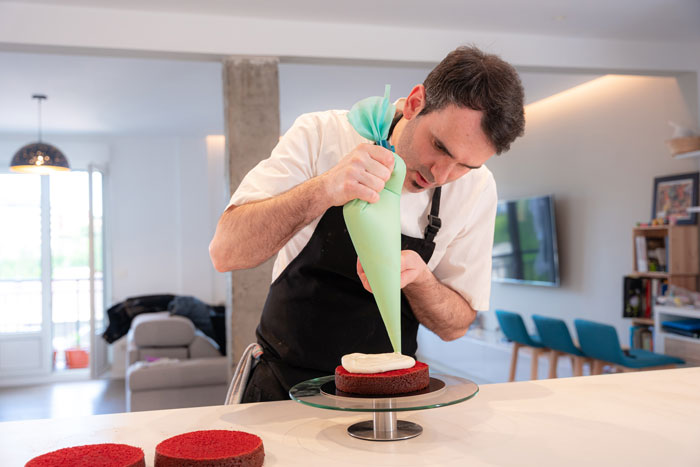 Baker decorando cuidadosamente el pastel en la cocina de casa, relacionado con el pastel gris y la preparación para la fiesta de revelación de género.