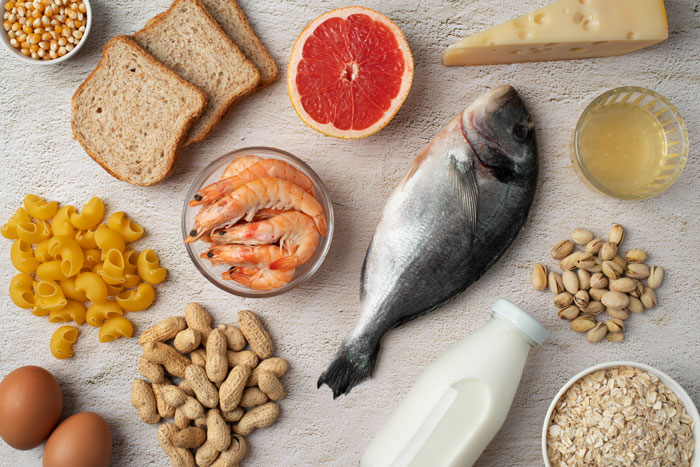 Varios alimentos alergénicos, como pescado, maní, leche, huevos y mariscos dispuestos en una superficie ligera.