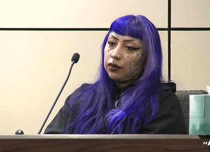 Mujer con cabello azul y tatuajes faciales sentados en la sala del tribunal durante la audiencia sobre el supuesto plan de disparo escolar masivo.