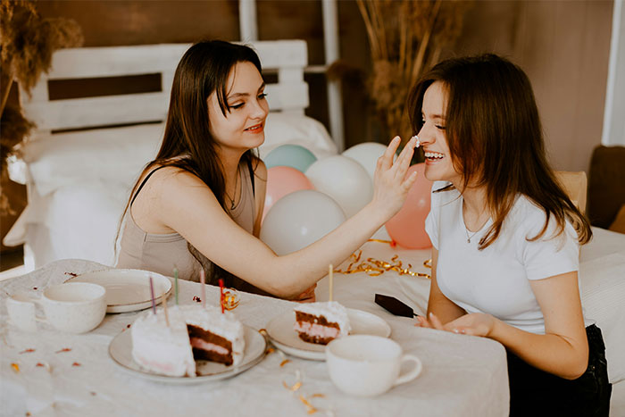 Dos mujeres que celebran un cumpleaños con pastel y globos, destacando la sorpresa de cumpleaños de un esposo, lo que lleva a la terapia.