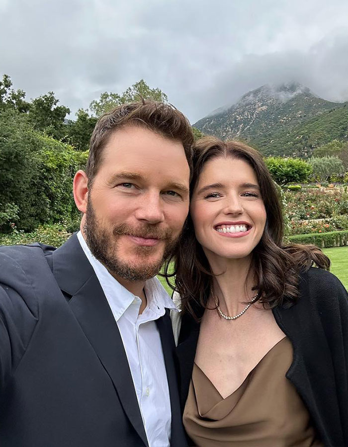Chris Pratt y la mujer sonriendo al aire libre con jardín verde y montaña en el fondo, relacionados con el caso de alquiler de alquiler de propiedades de Katy Perry.