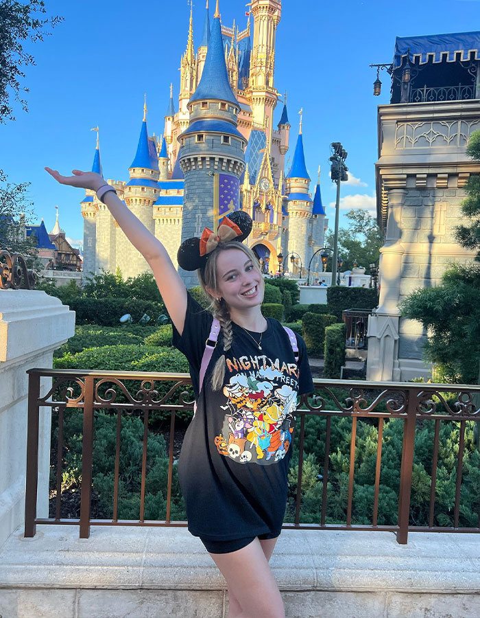 Mujer joven con orejas de ratón Minnie posa felizmente frente al Castillo de Disney World en medio de un giro impactante en el violento incidente de Disney World.
