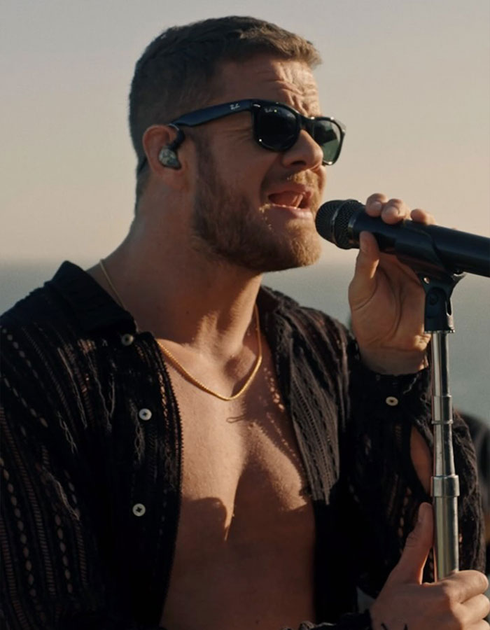 Dan Reynolds sin camisa en el escenario cantando en un micrófono, vistiendo gafas de sol, vinculando a la discusión de masculinidad tóxica.