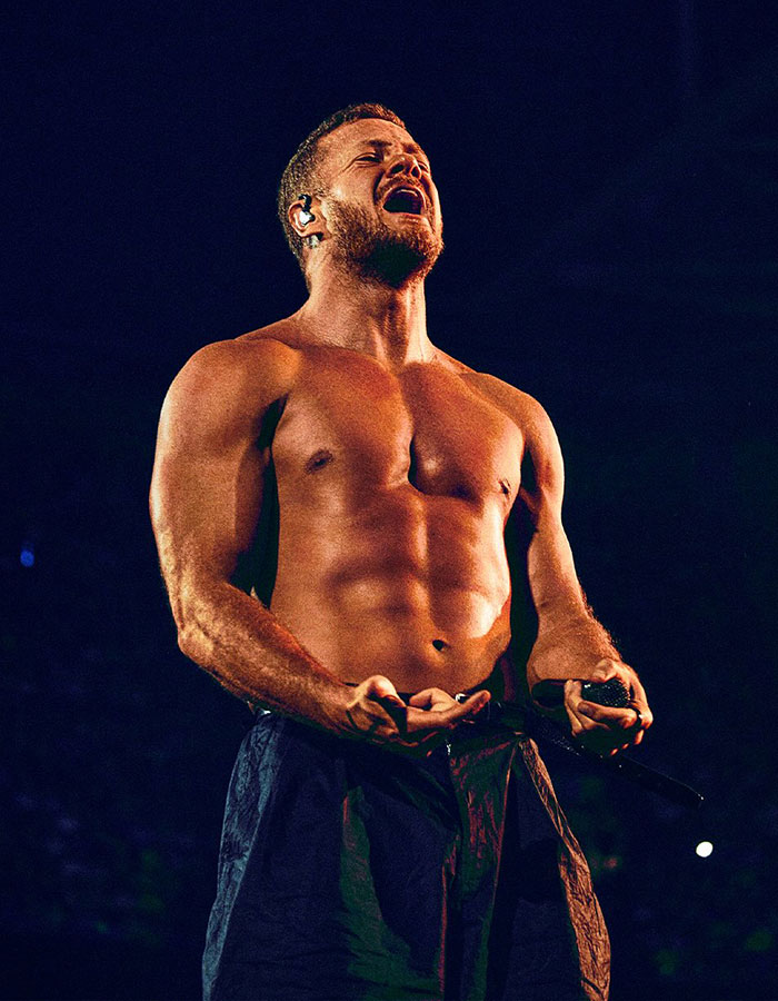 Dan Reynolds sin camisa en el escenario durante una presentación en vivo, destacando temas de masculinidad tóxica y autoexpresión.