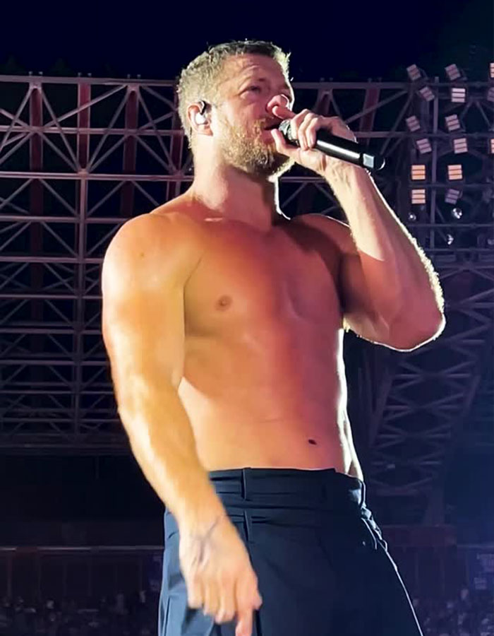 Dan Reynolds sin camisa en el escenario, sosteniendo un micrófono, destacando problemas en torno a la masculinidad tóxica en el rendimiento.