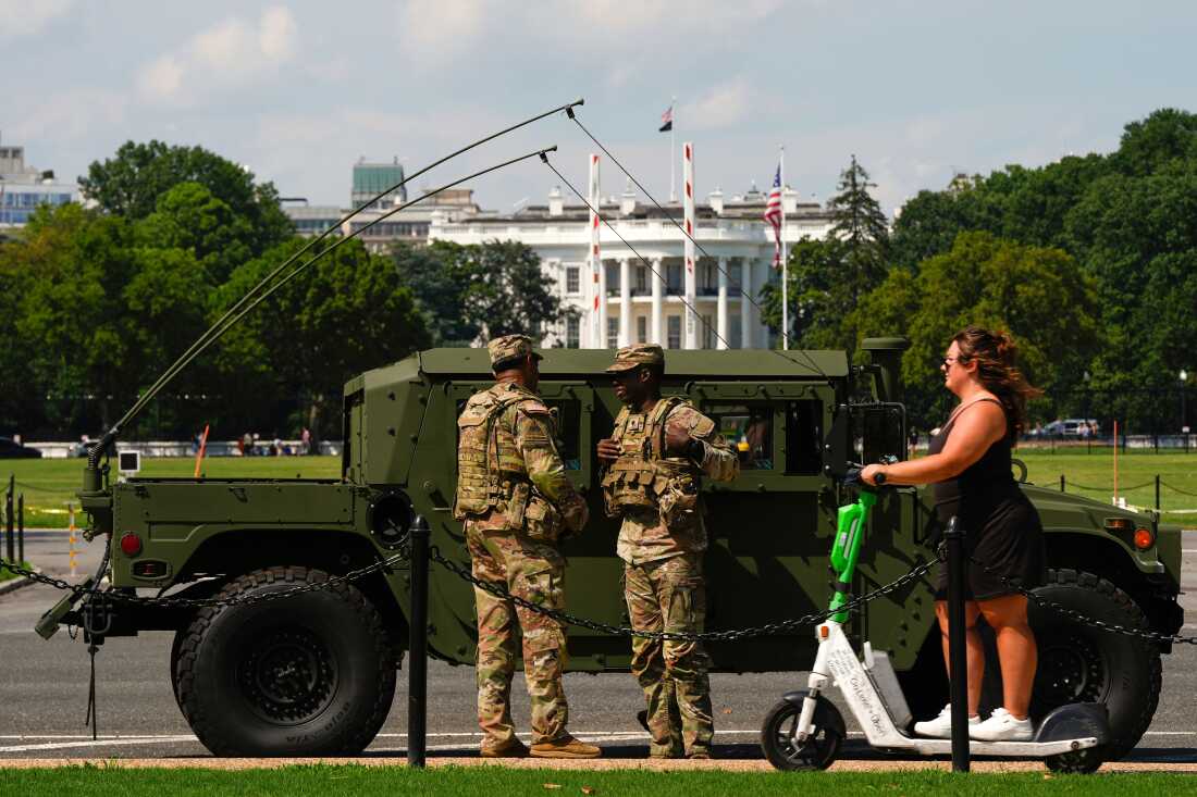 Miembros de la Patrulla de la Guardia Nacional del Distrito de Columbia frente a la Casa Blanca cuando una mujer pasa por un scooter, el sábado 16 de agosto de 2025, en Washington.