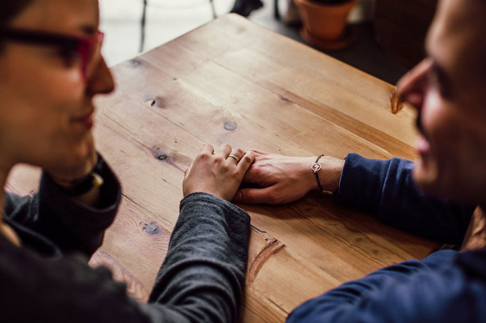 Pareja tomada de la mano sobre una mesa de madera, que representa la conexión emocional y el apoyo durante la discusión posparto.