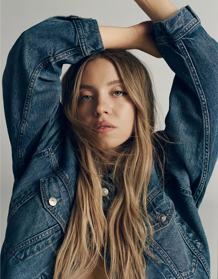 Mujer joven con cabello largo y rubio con una chaqueta de mezclilla posando para la campaña publicitaria de Jeans Gap.