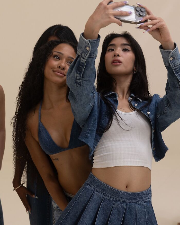 Dos mujeres con atuendos de mezclilla, posando para una selfie en un escenario de anuncios de jeans de brecha casual.