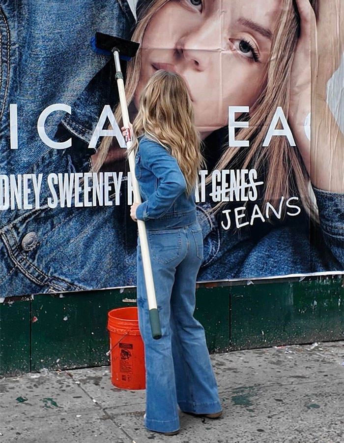 Mujer con jeans y chaqueta de mezclilla limpiando un gran anuncio de jeans de águila americana en una acera de la ciudad.