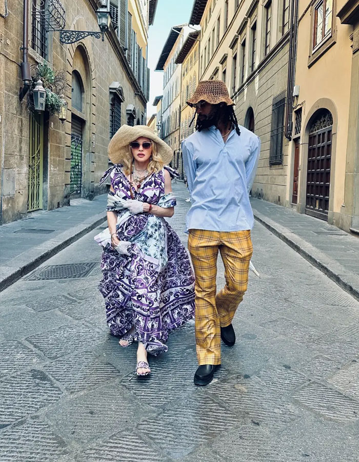 Madonna caminando con su novio con atuendos de estilo vintage en una calle adoquín, abrazando el consejo de cambio cosmético.