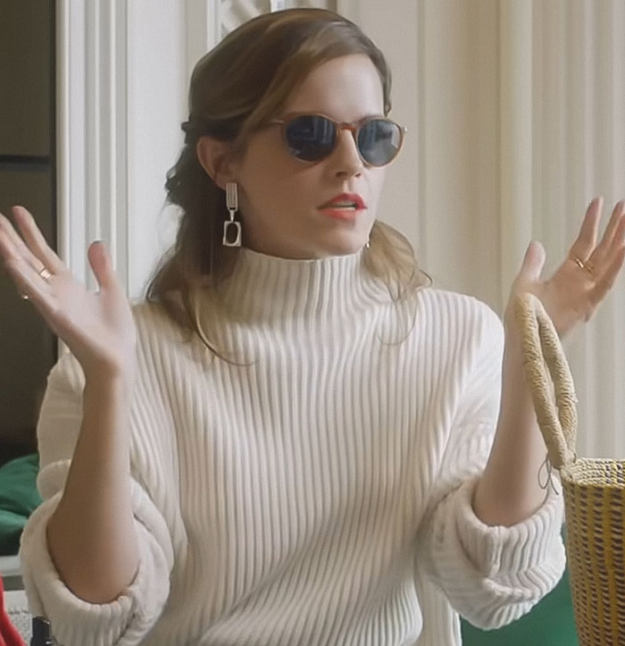 Mujer con gafas de sol y un suéter de acanalado blanco que gestiza en el interior, relacionado con Emma Watson usa un vestido transparente en una caminata.