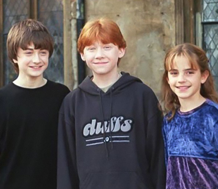 Tres jóvenes actores sonriendo juntos en el set, no relacionados con Emma Watson con un vestido transparente en una caminata.