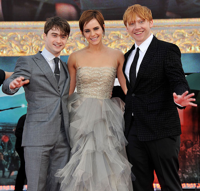 Los actores Daniel Radcliffe, Emma Watson y Rupert Grint posan juntos en un evento formal con elegante atuendo.