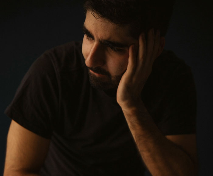 Young Man con una camisa oscura mirando cuidadosamente, reflexionando sobre los resultados mixtos de prueba de ADN en un entorno con poca luz.