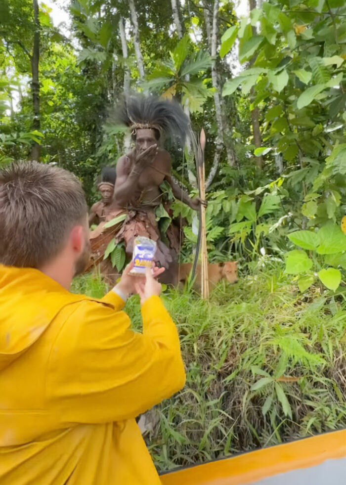 Influencer filmando miembro de la tribu indígena en atuendo tradicional en un entorno forestal para el truco viral de Tiktok.