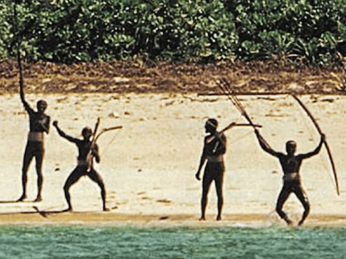 Tribu indígena de pie en una playa que sostiene arcos y flechas, destacando la controversia sobre el truco viral de Tiktok Filming de Influencer.