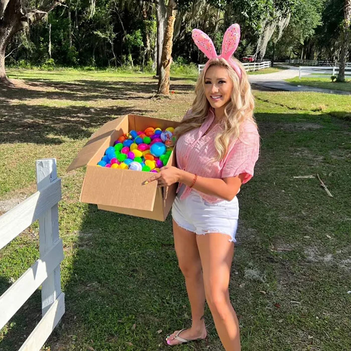 Modelo que posa al aire libre sosteniendo una caja de bolas coloridas, con orejas de conejo y ropa casual de verano, gran discriminación de senos.