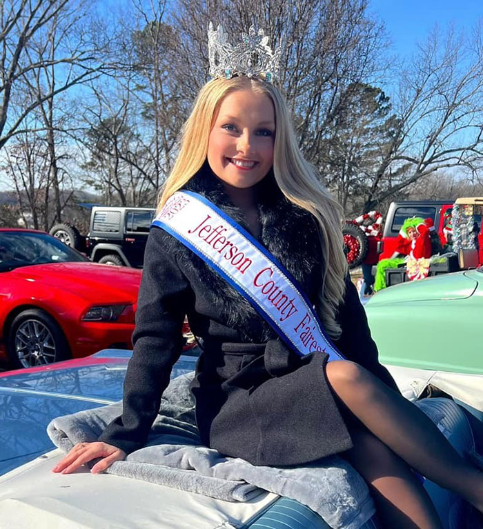 Mujer joven que usa una corona y una faja en un evento al aire libre, relacionado con publicaciones en las redes sociales sobre la maternidad.