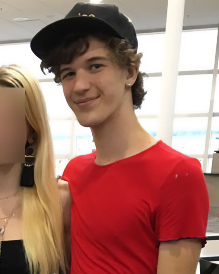 Young Man con camisa roja y gorra negra de pie en el interior de una mujer con cara borrosa, conectada a la historia sospechosa de Minneapolis.