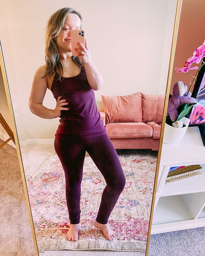 Mujer de 31 años con enanismo con atuendo púrpura tomando una selfie espejo que muestra su transformación de cirugía de altura.