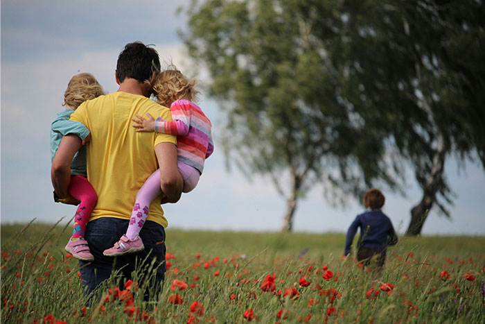 Hombre que lleva a dos jóvenes en un campo de flores rojas mientras un niño camina por delante, ilustrando temas familiares y abandonados de hijo.