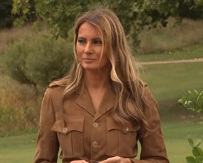 Melania Trump con una chaqueta marrón al aire libre, reflejando mensajes ocultos detrás de las opciones de vestuario durante la visita al estado del Reino Unido.