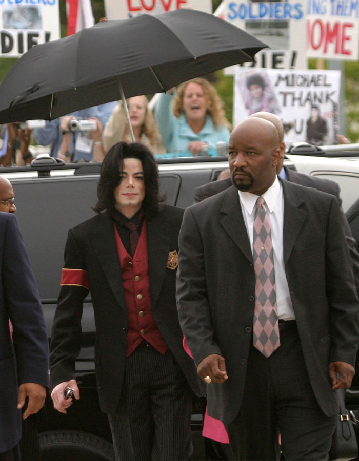 Michael Jackson caminando con seguridad, rodeado de fanáticos y letreros, destacando historias de vida íntimas de Priscilla Presley.