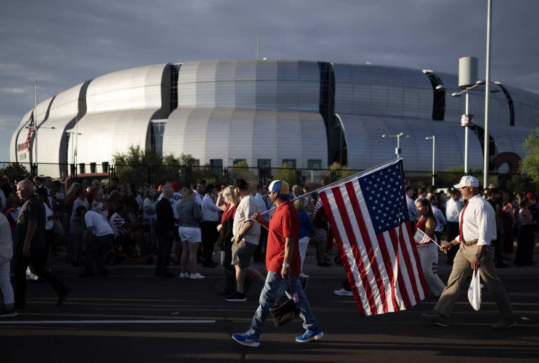 Un hombre lleva una bandera estadounidense cuando las personas llegan al servicio público conmemorativo del activista de derecha Charlie Kirk en el Estadio State Farm en Glendale, Arizona, el 21 de septiembre de 2025.