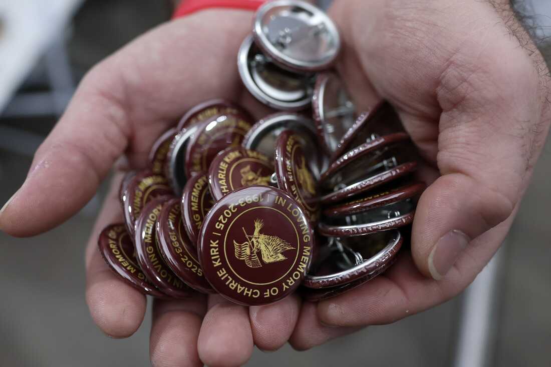 Un hombre muestra pines mientras los asistentes se reúnen en los grados por delante del servicio conmemorativo para el activista político Charlie Kirk en el Estadio State Farm el 21 de septiembre de 2025 en Glendale, Arizona.