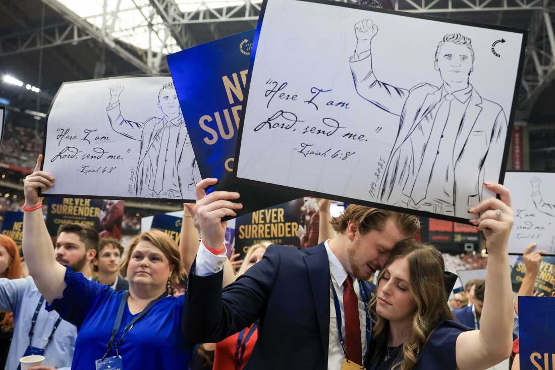 Los asistentes sostienen letreros religiosos en el servicio conmemorativo para el activista político Charlie Kirk.